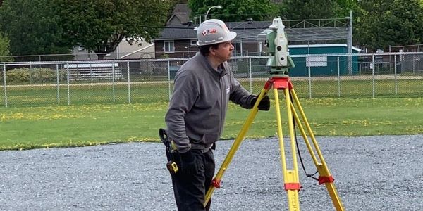 Surveyor using leveling equipment on a sports field site for turf installation and ground preparation