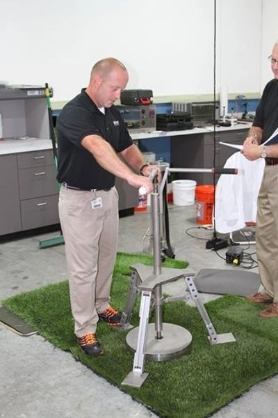 Technician performing synthetic turf impact testing using specialized lab equipment for surface safety evaluation