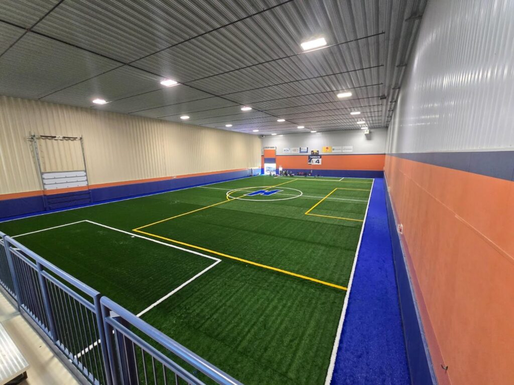 Large indoor football training facility with synthetic turf field and performance training setup for athletes
